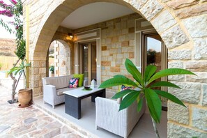 An outdoor seating area with wicker furniture, stone walls, and potted plants. - Nikolas Villas Kamilari (Faistos)