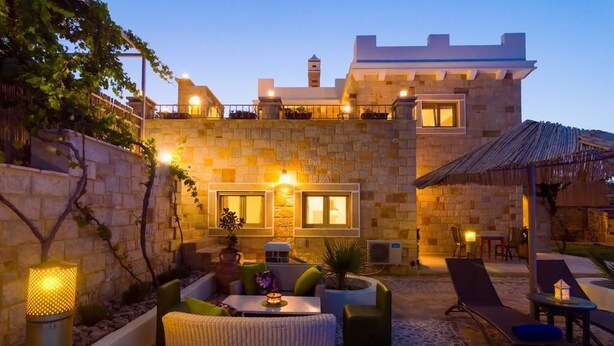 A stone building with a courtyard featuring outdoor seating, a small pool, and a thatched roof structure. - Nikolas Villas Kamilari (Faistos)