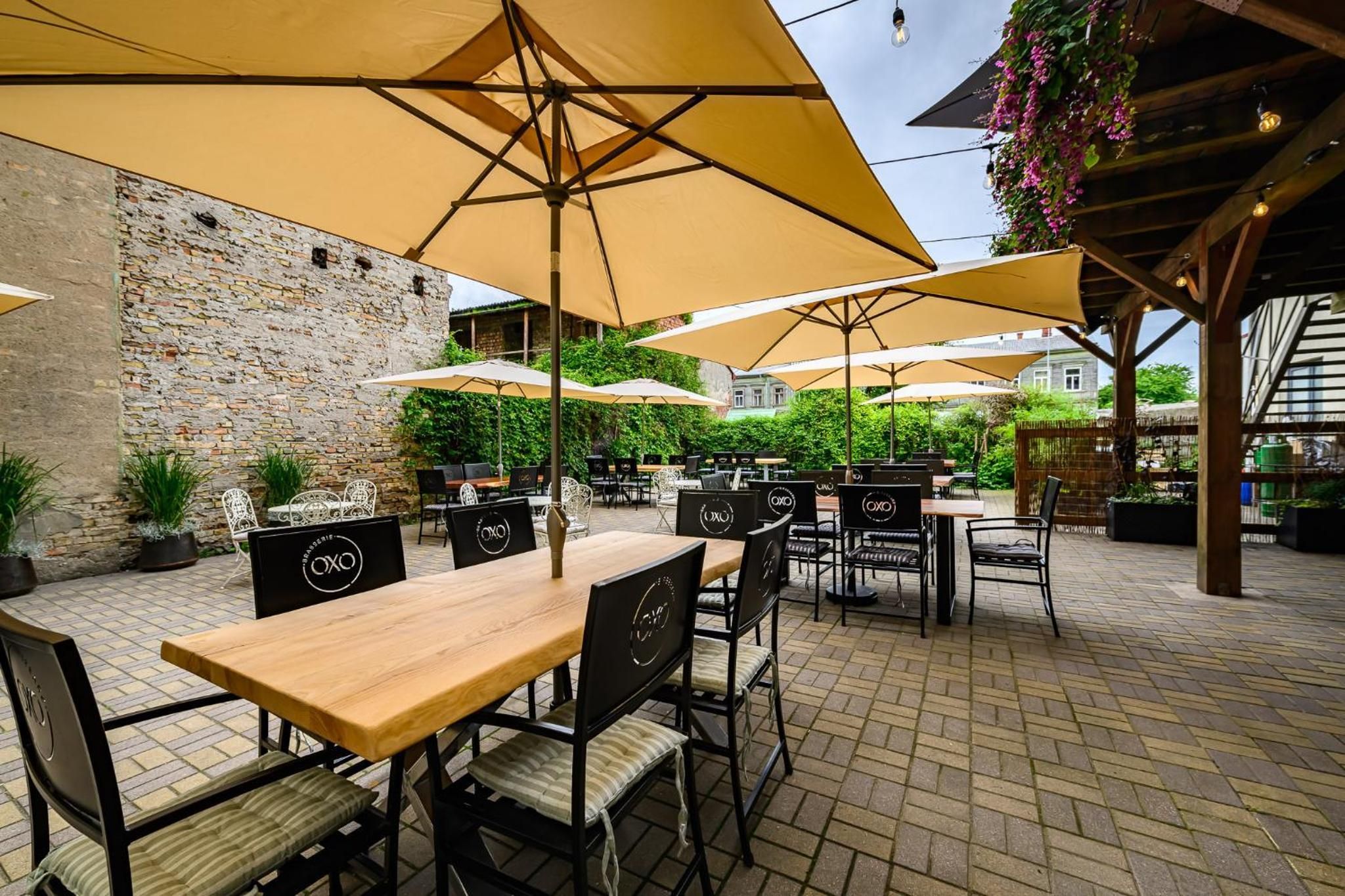 Un patio al aire libre con mesas y sillas, cubierto por grandes sombrillas, y un muro de piedra al fondo.