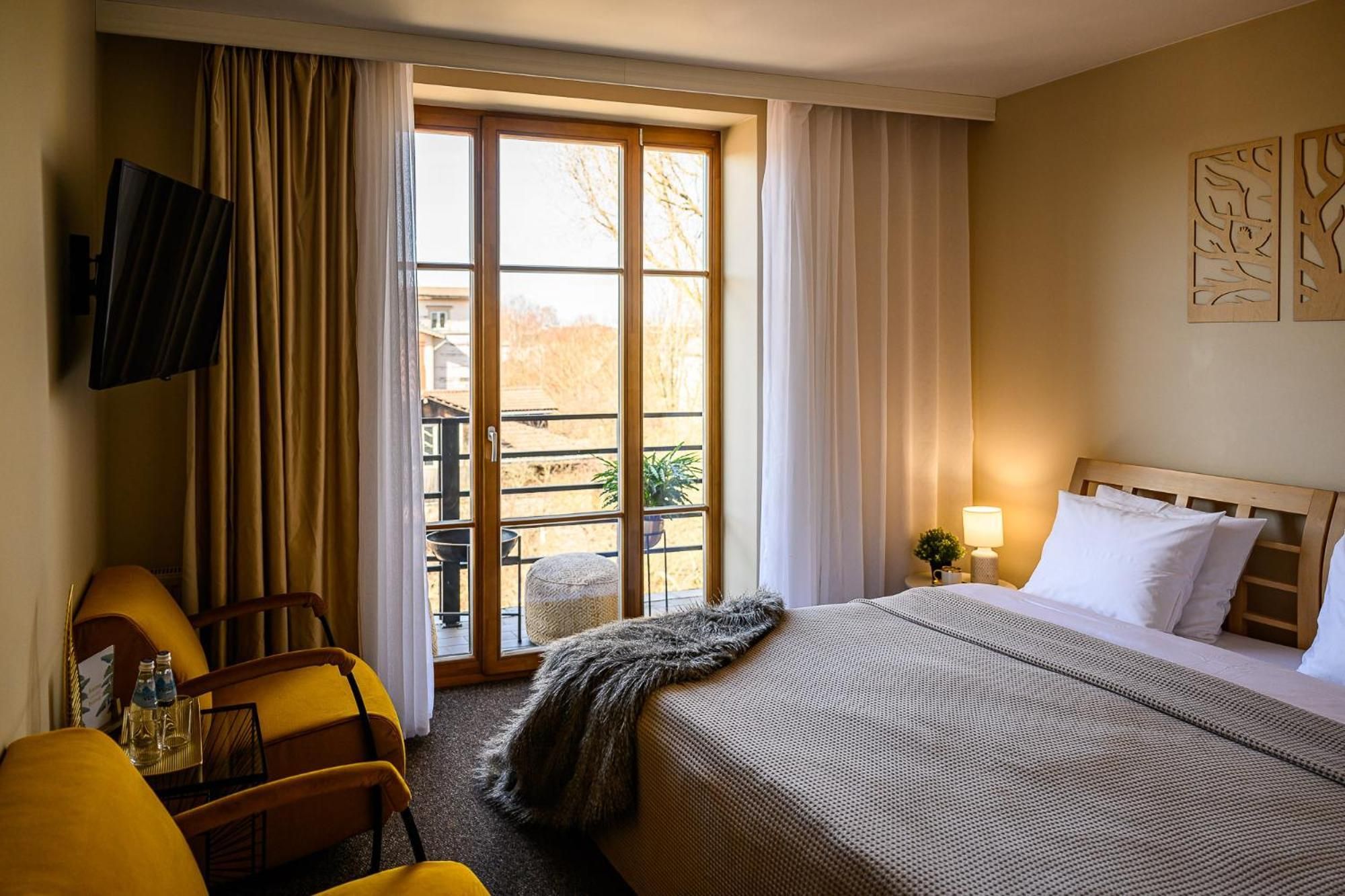 A hotel room with a bed, a chair, a TV, a window with curtains, and a view of the outside.
