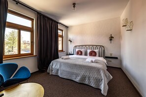 Un dormitorio con cama, una silla, un escritorio y una ventana con cortinas.