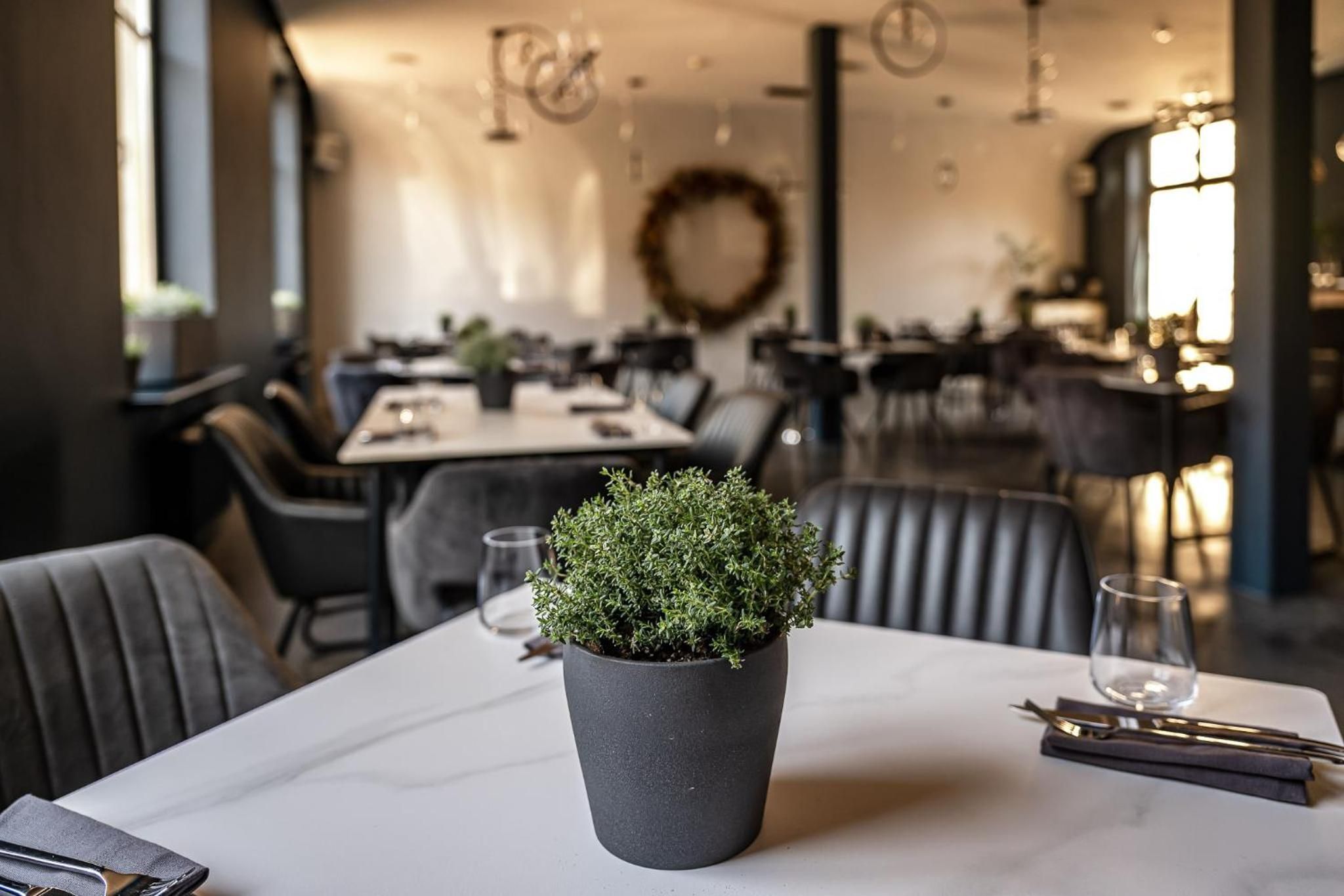 A restaurant interior with a table set for dining, a potted plant, and a dining area with chairs and tables.