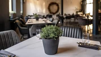 A restaurant interior with a table set for dining, a potted plant, and a dining area with chairs and tables.