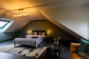 Un dormitorio moderno con techo inclinado, cama con cabecera geométrica, una mesita de noche pequeña, una mesa de centro y vista al cielo a través de un tragaluz.
