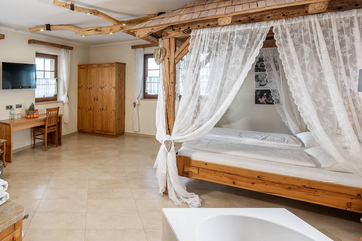 Un dormitorio con una cama con dosel de madera, un escritorio de madera, una silla, un armario y un televisor en la pared.