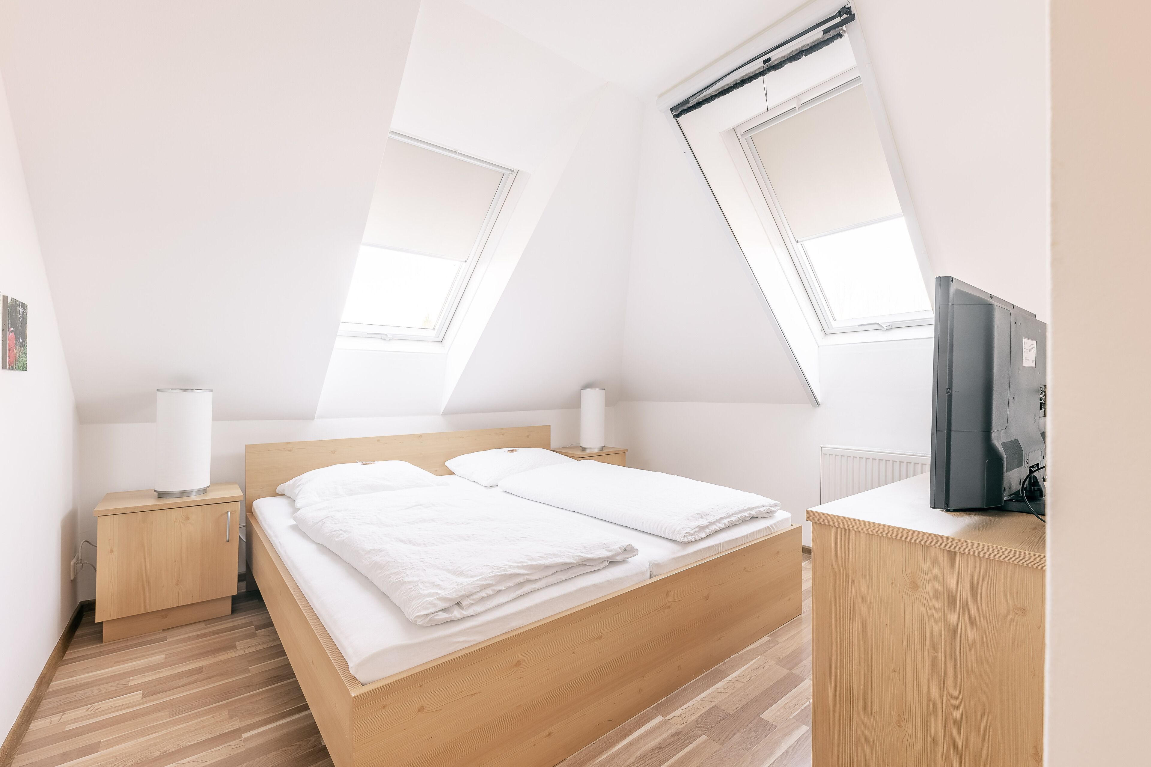 A modern bedroom with a wooden bed, a nightstand, a desk, and a TV.