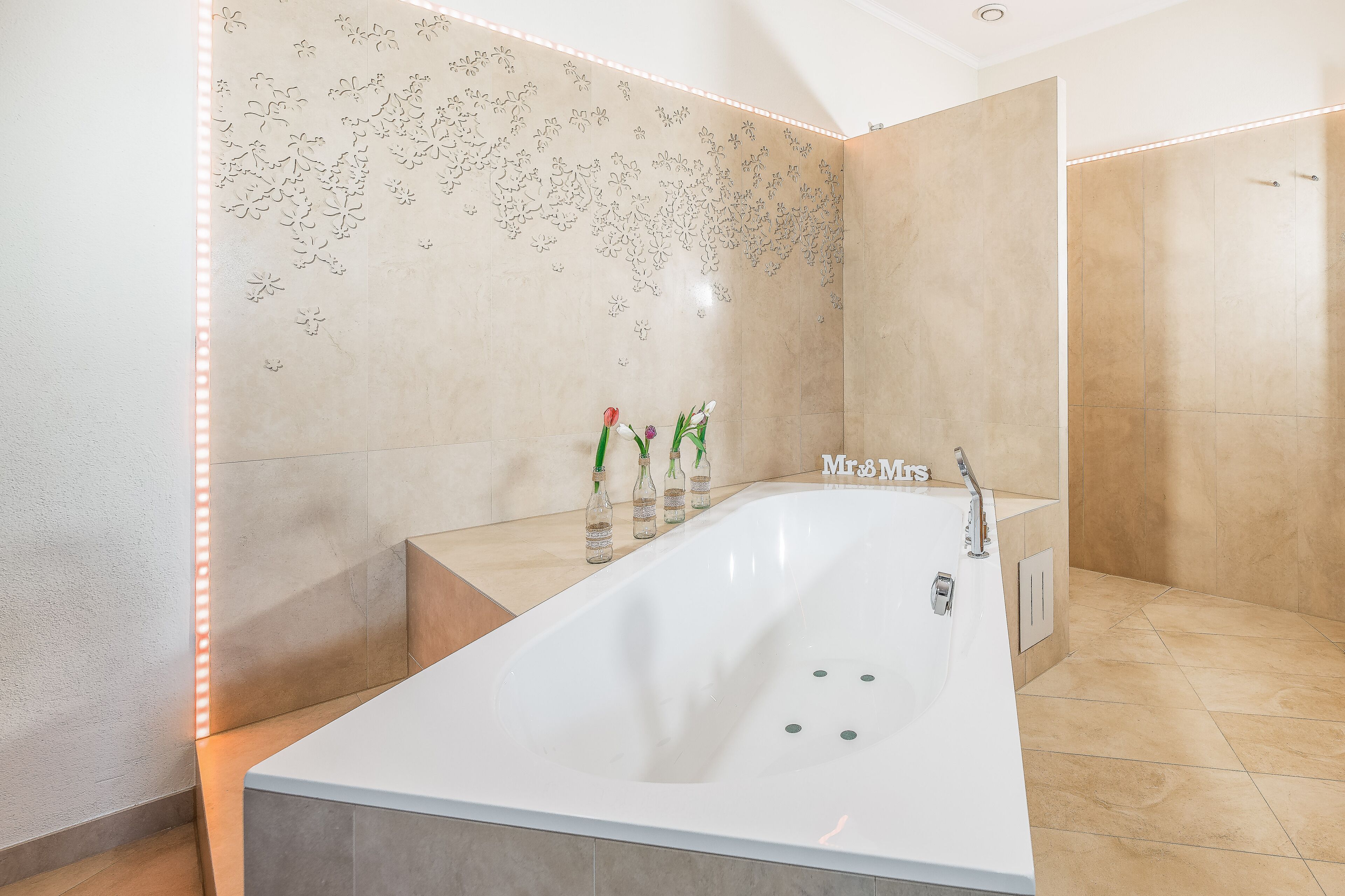 Un baño moderno con una bañera grande, zona de ducha y una pared decorativa con motivos florales.