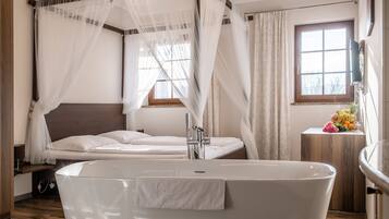 Un dormitorio moderno con una bañera grande, cabecera de madera y una ventana con cortinas.