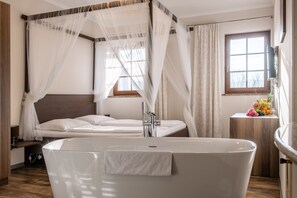 Ein modernes Schlafzimmer mit einer großzügigen Badewanne, einem hölzernen Kopfteil und einem Fenster mit Vorhängen.
