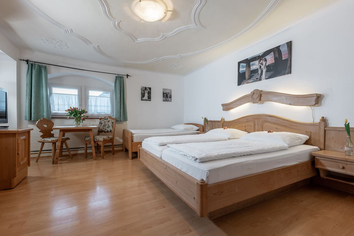 Habitación de hotel con dos camas de madera, un escritorio con silla, un televisor y una ventana con cortinas.