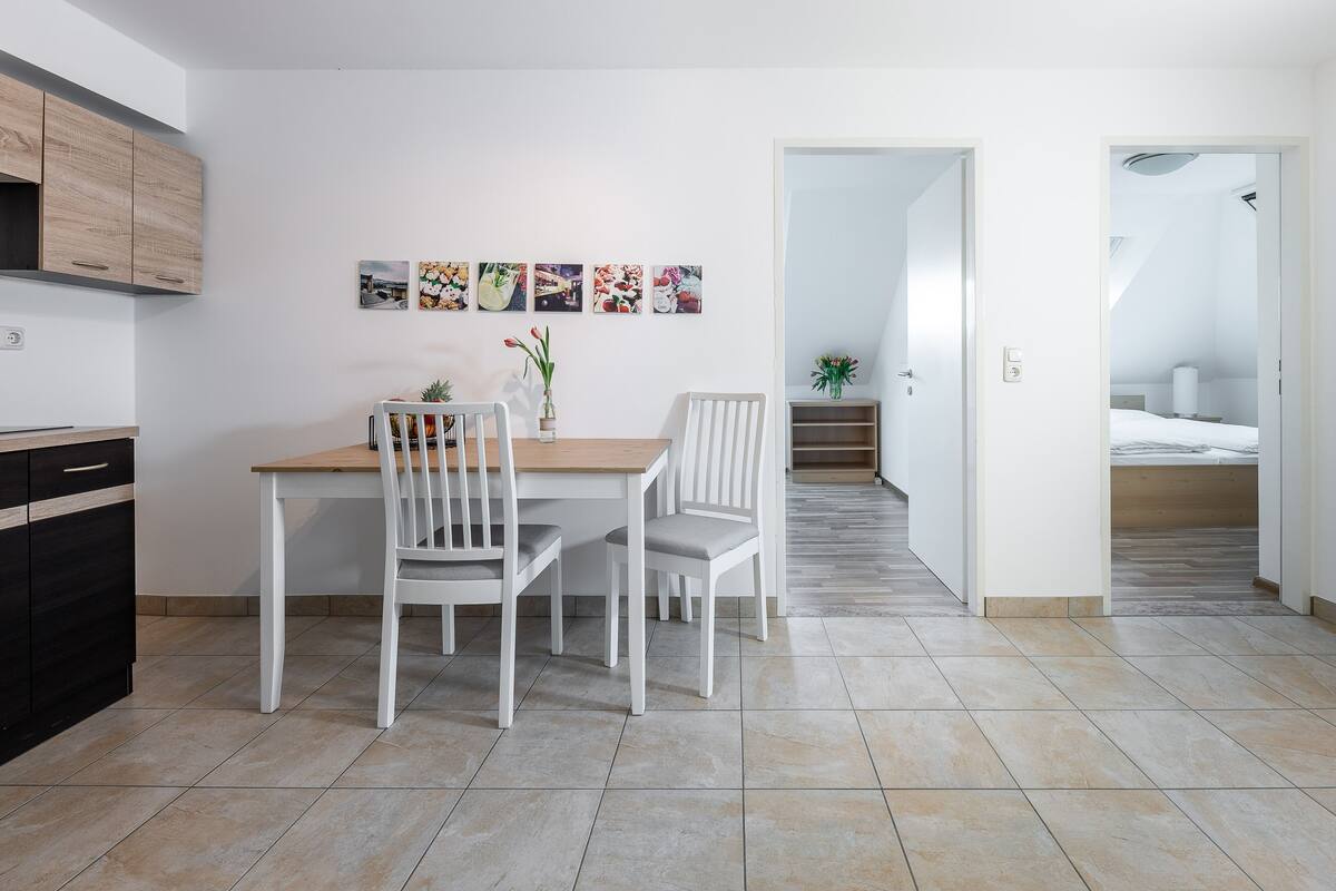 Una cocina moderna con armarios blancos y una zona de comedor con una mesa de madera y sillas blancas.