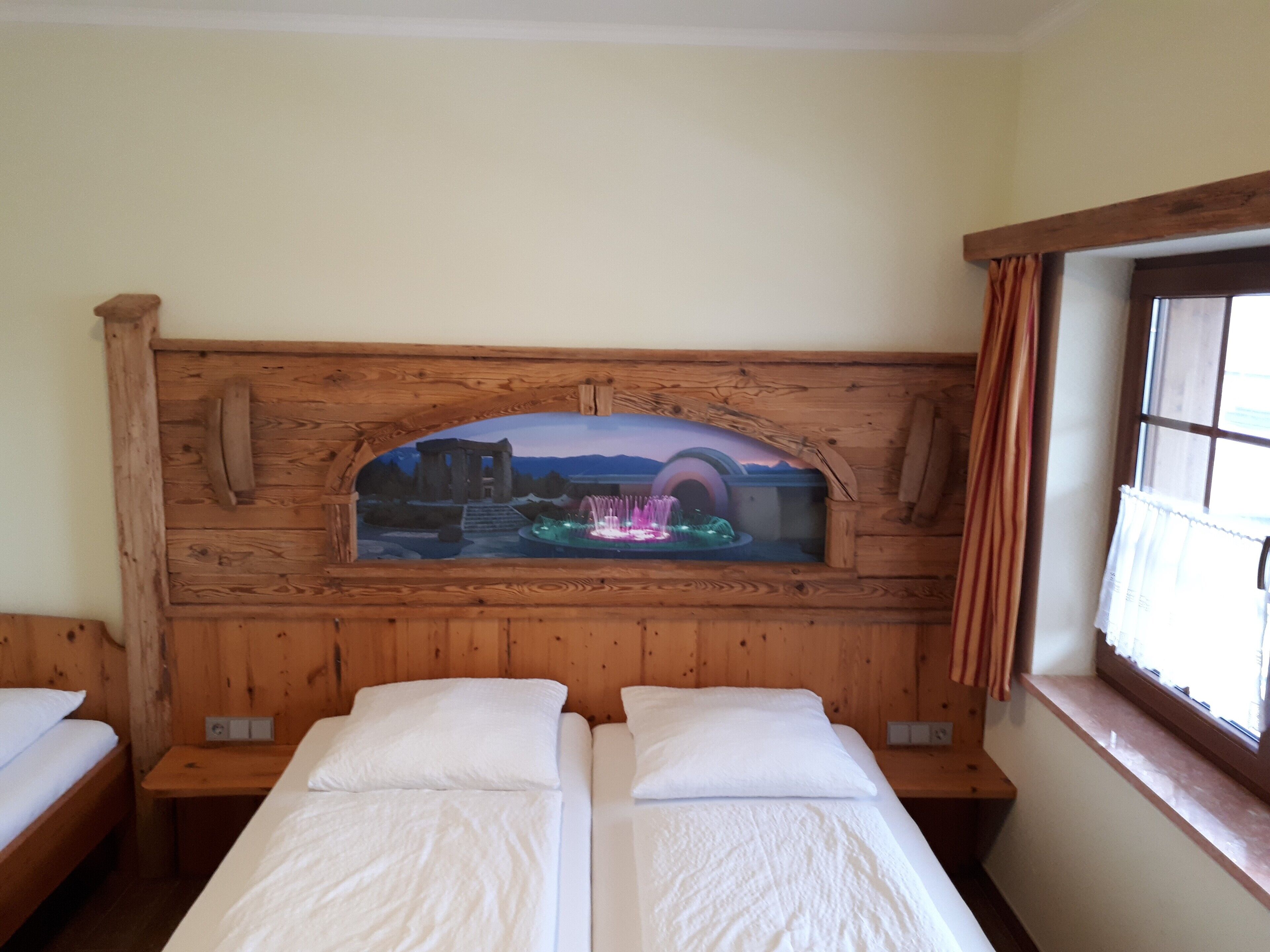 A room with two beds, a wooden headboard with a decorative arch, and a window with curtains.