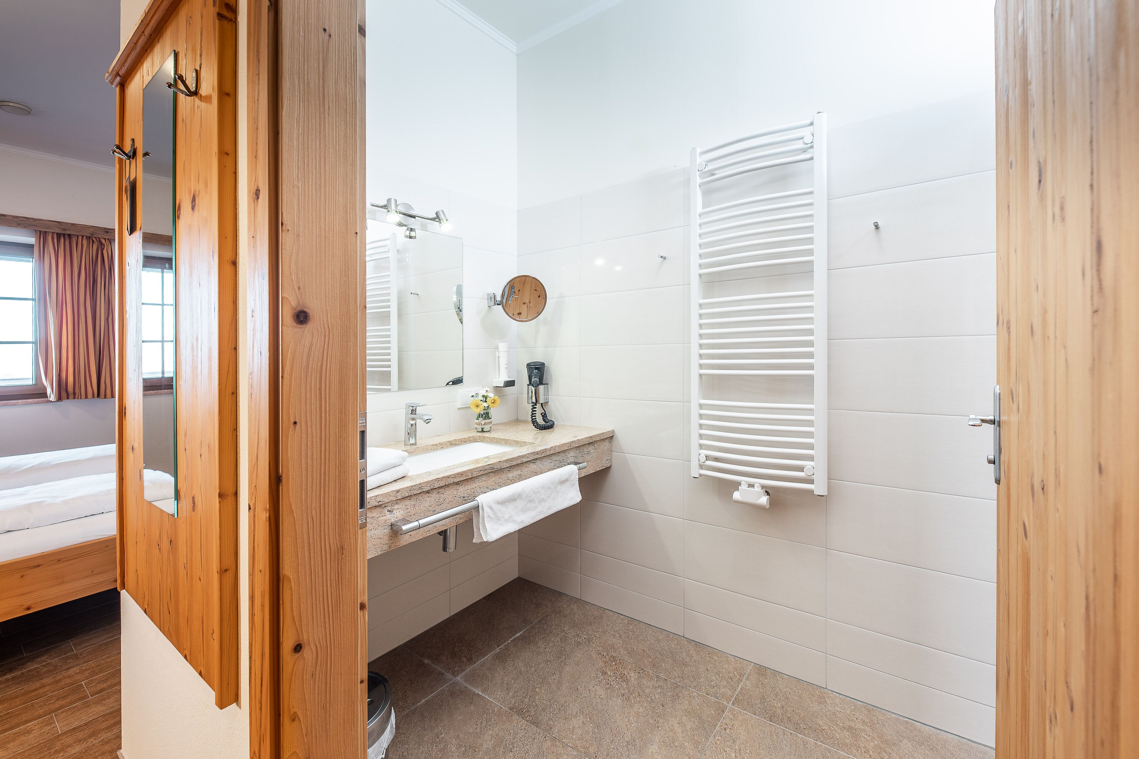 Un baño moderno con puerta de madera, un lavabo con toalla y un perchero blanco.