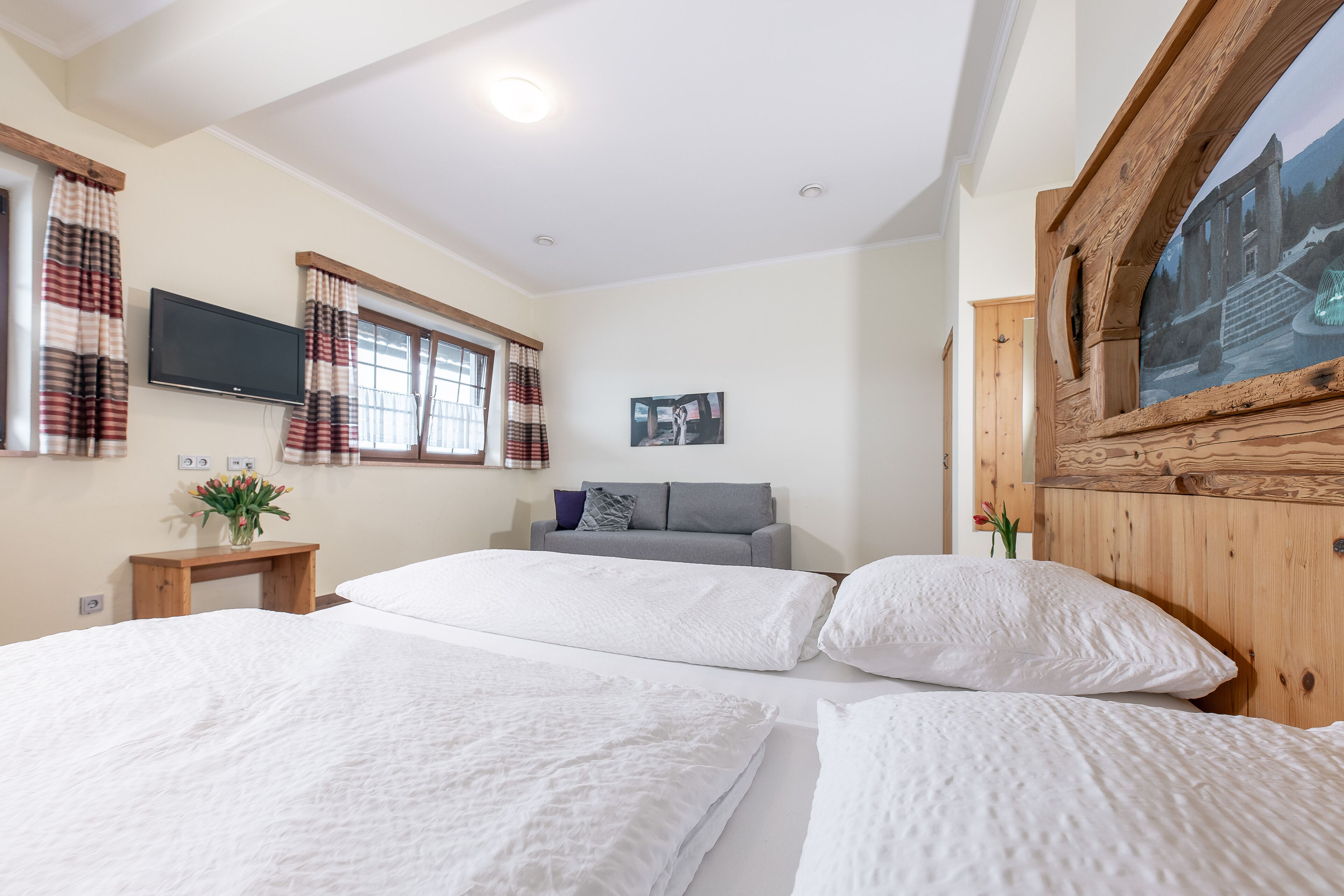 A bedroom with a large bed, a TV mounted on the wall, and a window with curtains.
