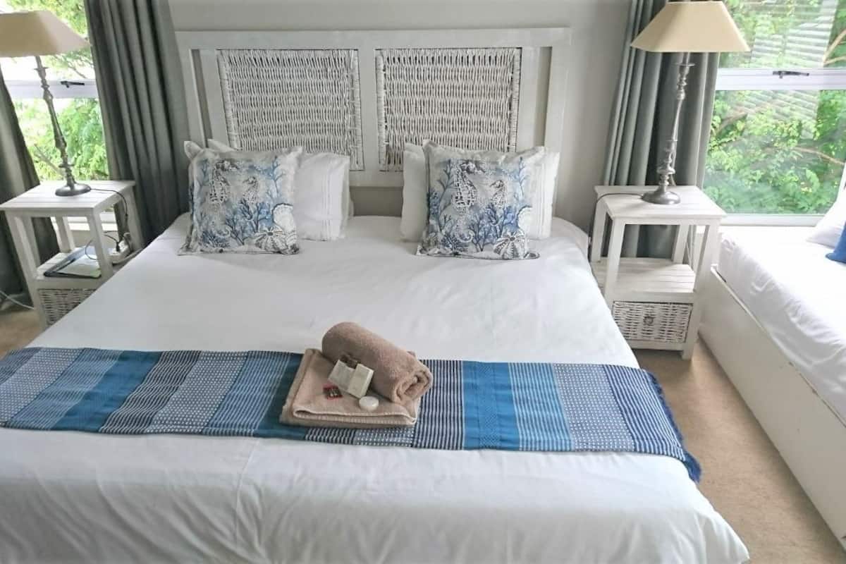 Une chambre d’hôtel avec un grand lit, deux tables de chevet, un ventilateur et une fenêtre avec des rideaux.
