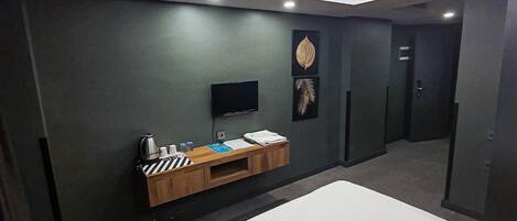 A modern hotel room with a bed, a small wooden side table, a flat-screen TV, and a wall-mounted artwork.