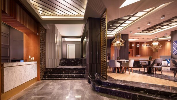 Un vestíbulo de hotel moderno con una escalera de mármol, un mostrador de recepción e iluminación contemporánea.