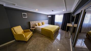 Habitación de hotel moderna con una cama grande, un sillón amarillo, una mesita de noche pequeña y un espejo amplio.