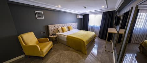 Habitación de hotel moderna con una cama grande, un sillón amarillo, una mesita de noche pequeña y un espejo amplio.