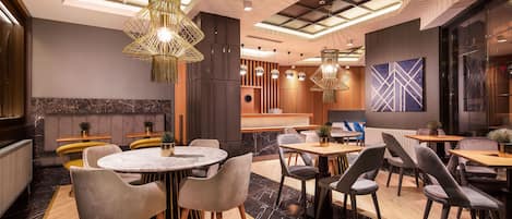A modern dining area with round tables and chairs, pendant lighting, and a large abstract painting on the wall.