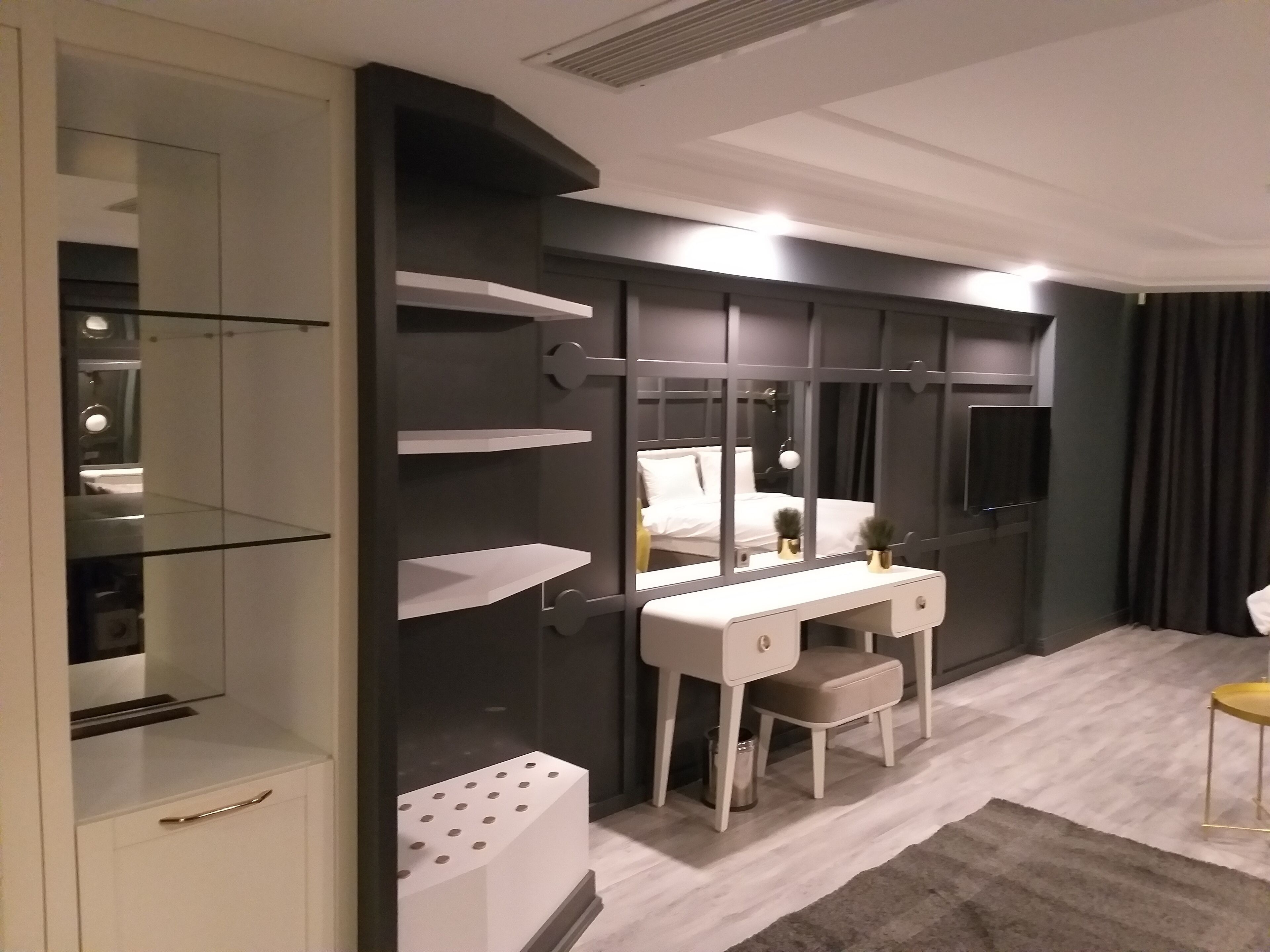 A modern bedroom with a vanity, a bed, and a TV.