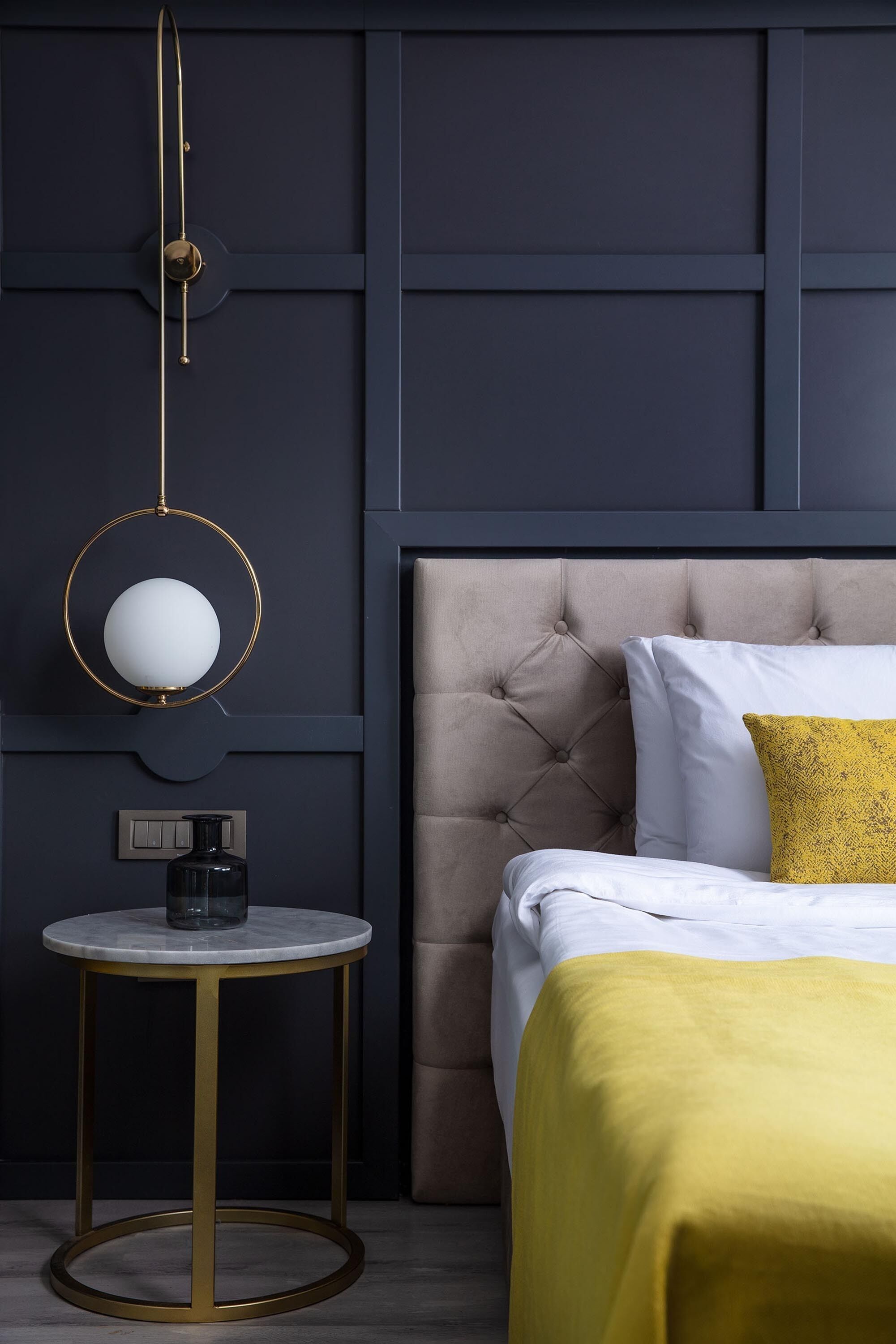 Una camera da letto con una testiera trapuntata, un tavolino con una lampada e un letto con coperta gialla.