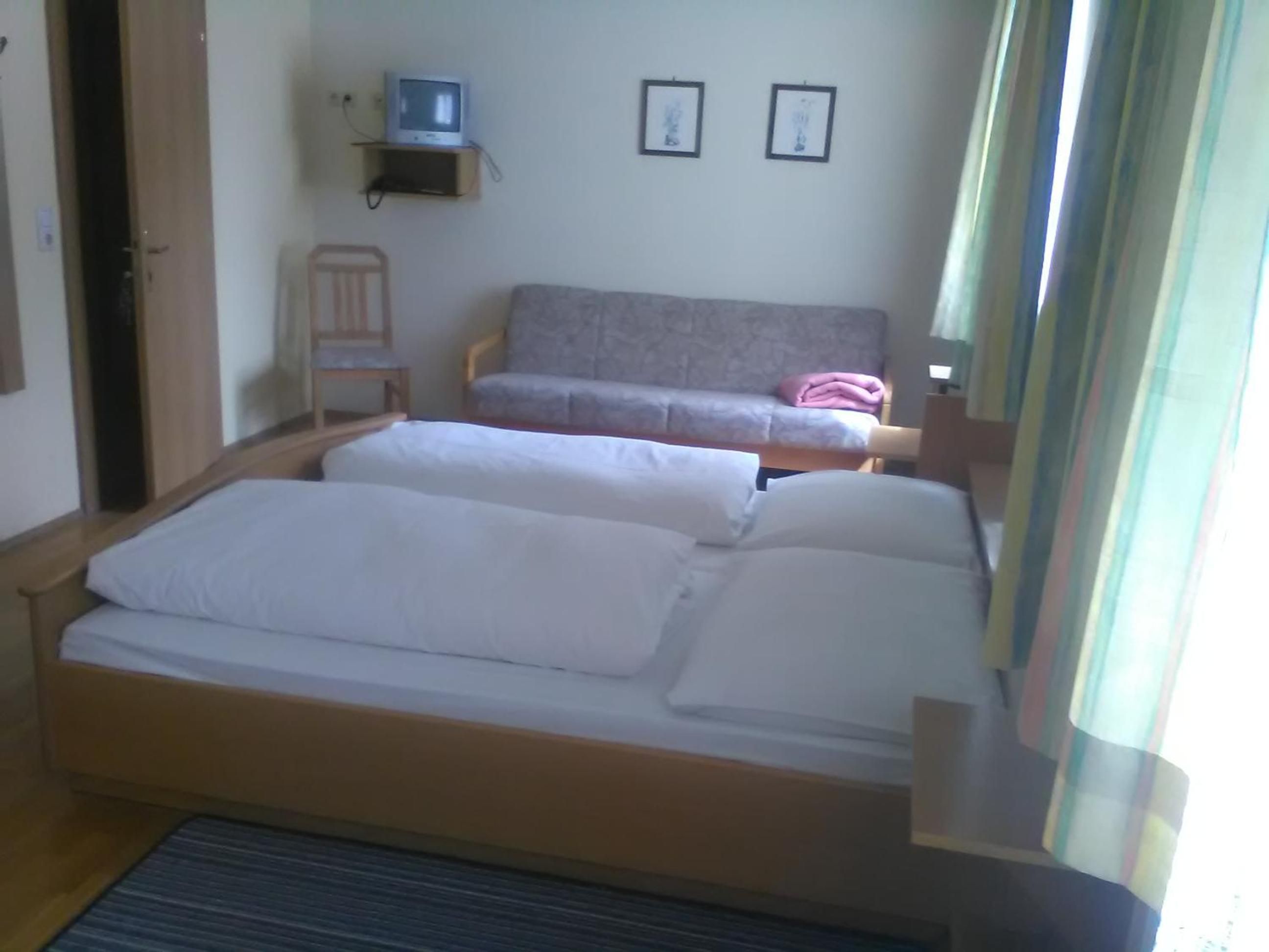 A room with two beds, a television on a shelf, and two framed pictures on the wall.