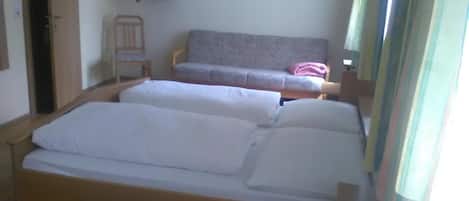 A room with two beds, a television on a shelf, and two framed pictures on the wall.