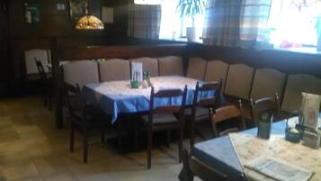 A dining area with a round table, chairs, and a bench. There are hanging lights and a potted plant.
