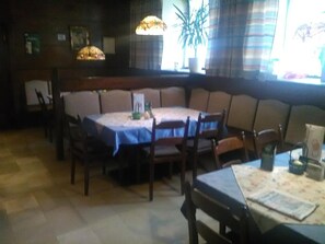 Un comedor con una mesa redonda, sillas y un banco. Hay lámparas colgantes y una planta en maceta.