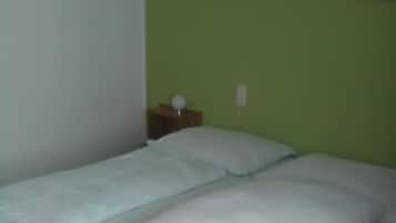Een eenpersoonskamer met een groene muur, een klein nachtkastje met een lamp, en twee posters.