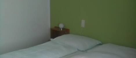 A single-bed room with a green wall, a small bedside table with a lamp, and two posters on the wall.
