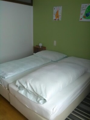A single-bed room with a green wall, a small bedside table with a lamp, and two posters on the wall.