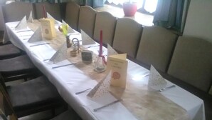 A long table with a white tablecloth, arranged with chairs, a vase with flowers, and a candle. - Gasthof Schatzl (Grieskirchen)