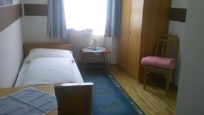 A hotel room with a bed, a desk, a chair, a wardrobe, and a window with curtains. - Gasthof Schatzl (Grieskirchen)