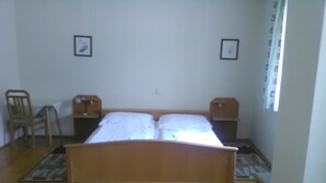 A bedroom with a wooden bed, two bedside tables, a chair, and a window with curtains. - Gasthof Schatzl (Grieskirchen)