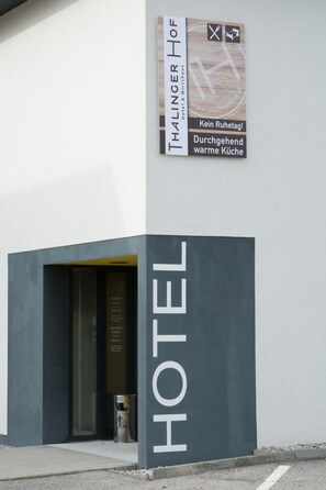 A hotel entrance with a sign that reads 'THALINGER HOF Hotel & Wirtshaus' and a slogan 'Kein Ruhetag! Durchgehend warme Küche'.