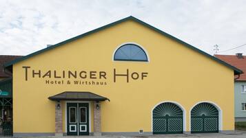 Um edifício amarelo com a placa 'Thalinger Hof Hotel & Wirtshaus' e duas portas duplas verdes.