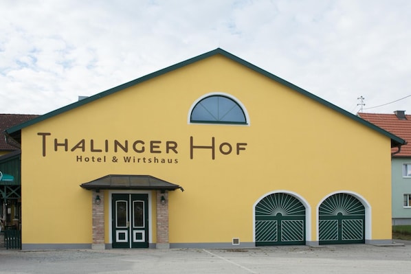 A yellow building with the sign 'Thalinger Hof Hotel & Wirtshaus' and two green double doors.