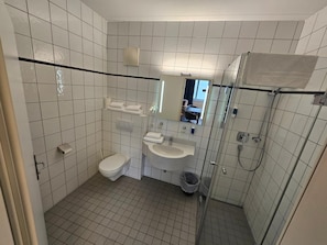 A small, tiled bathroom with a toilet, sink, and shower. - Thalinger Hof (Kronstorf)