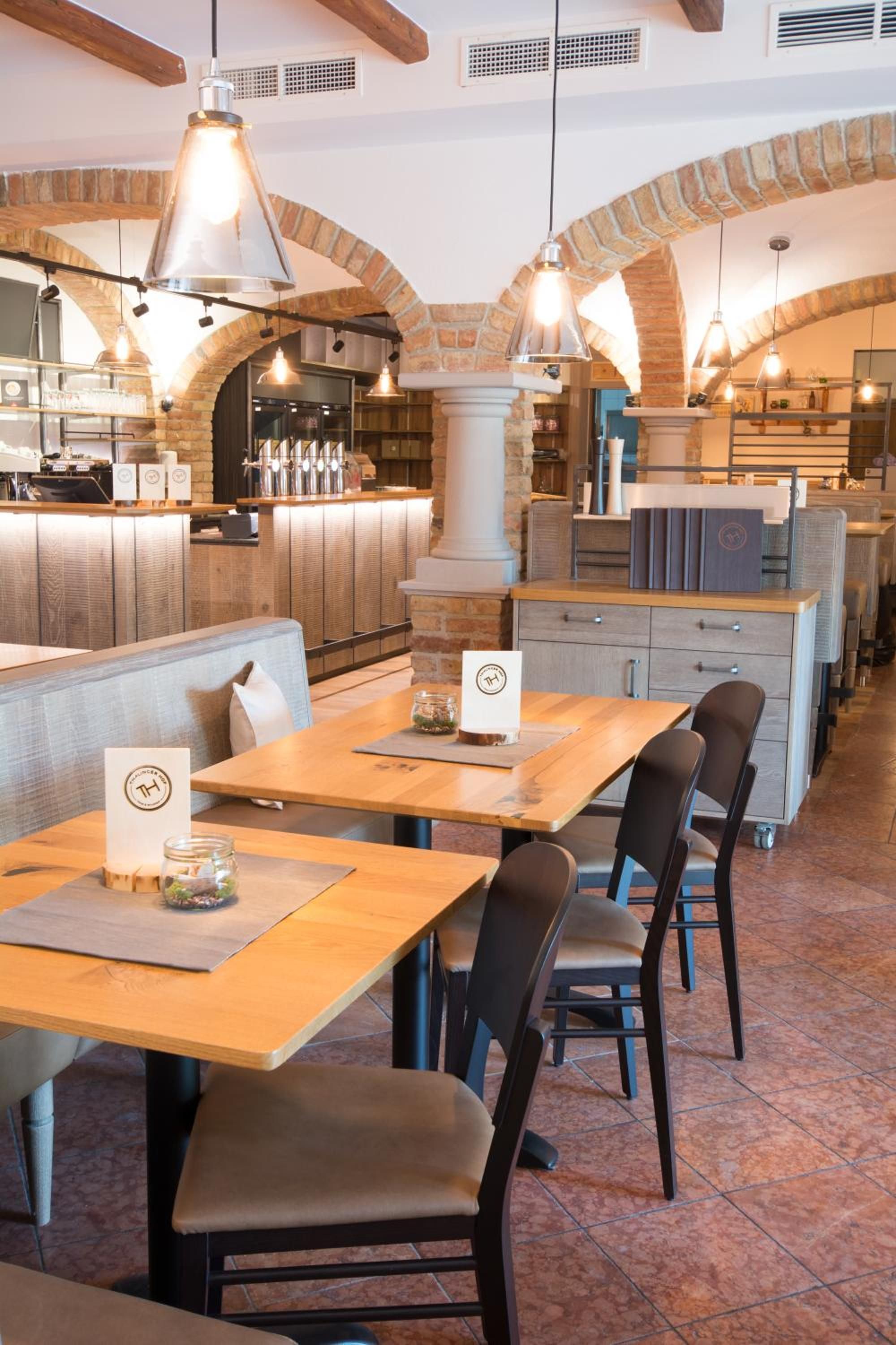 A restaurant interior with wooden tables, chairs, and hanging pendant lights.
