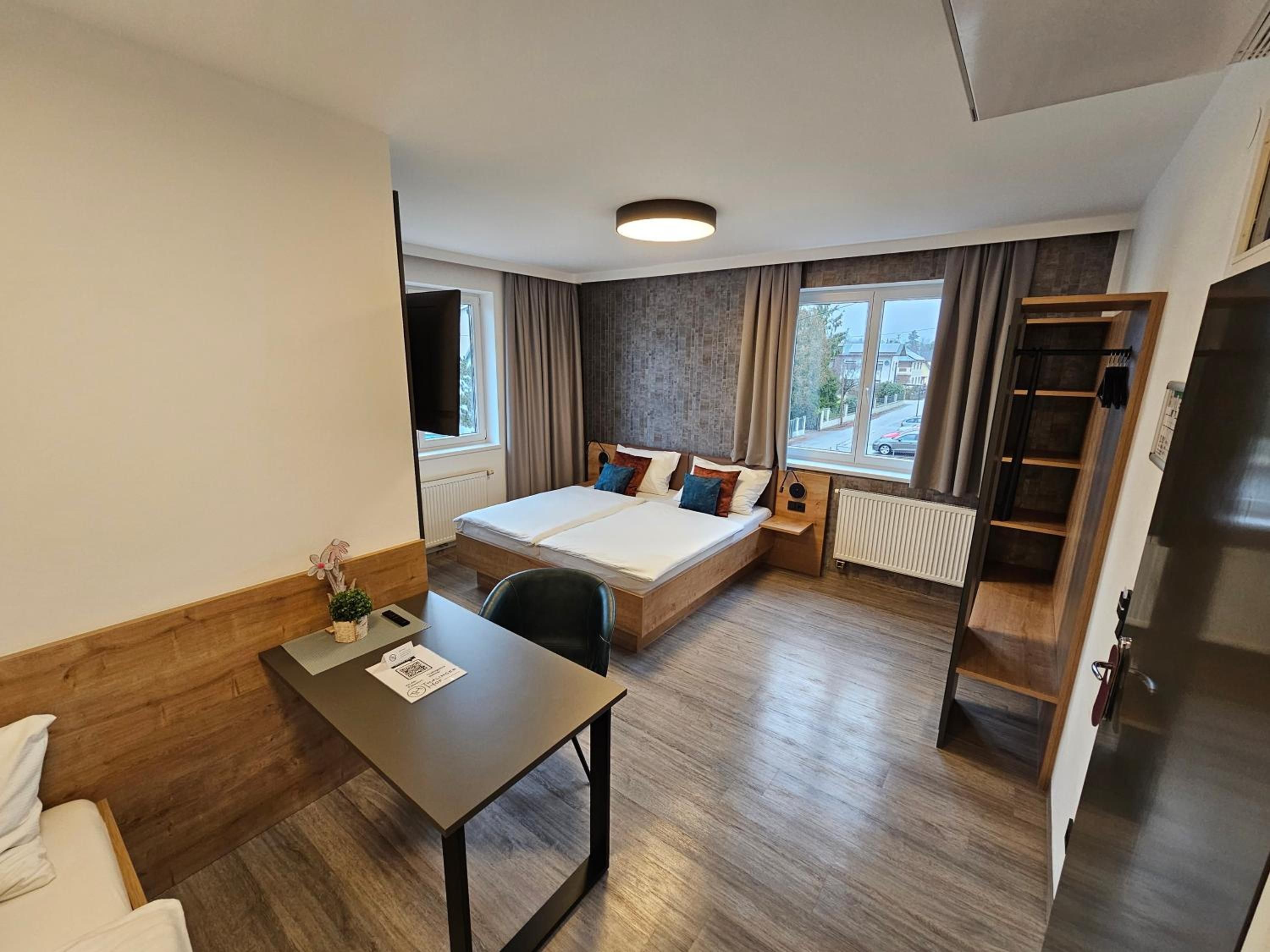 Ein modernes Hotelzimmer mit Bett, Schreibtisch, Stuhl, einem Fenster mit Vorhängen und Blick nach draußen.