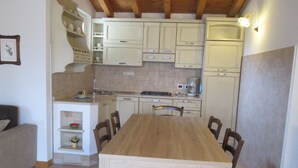 A compact kitchen with white cabinets, a wooden dining table, and a coffee maker.