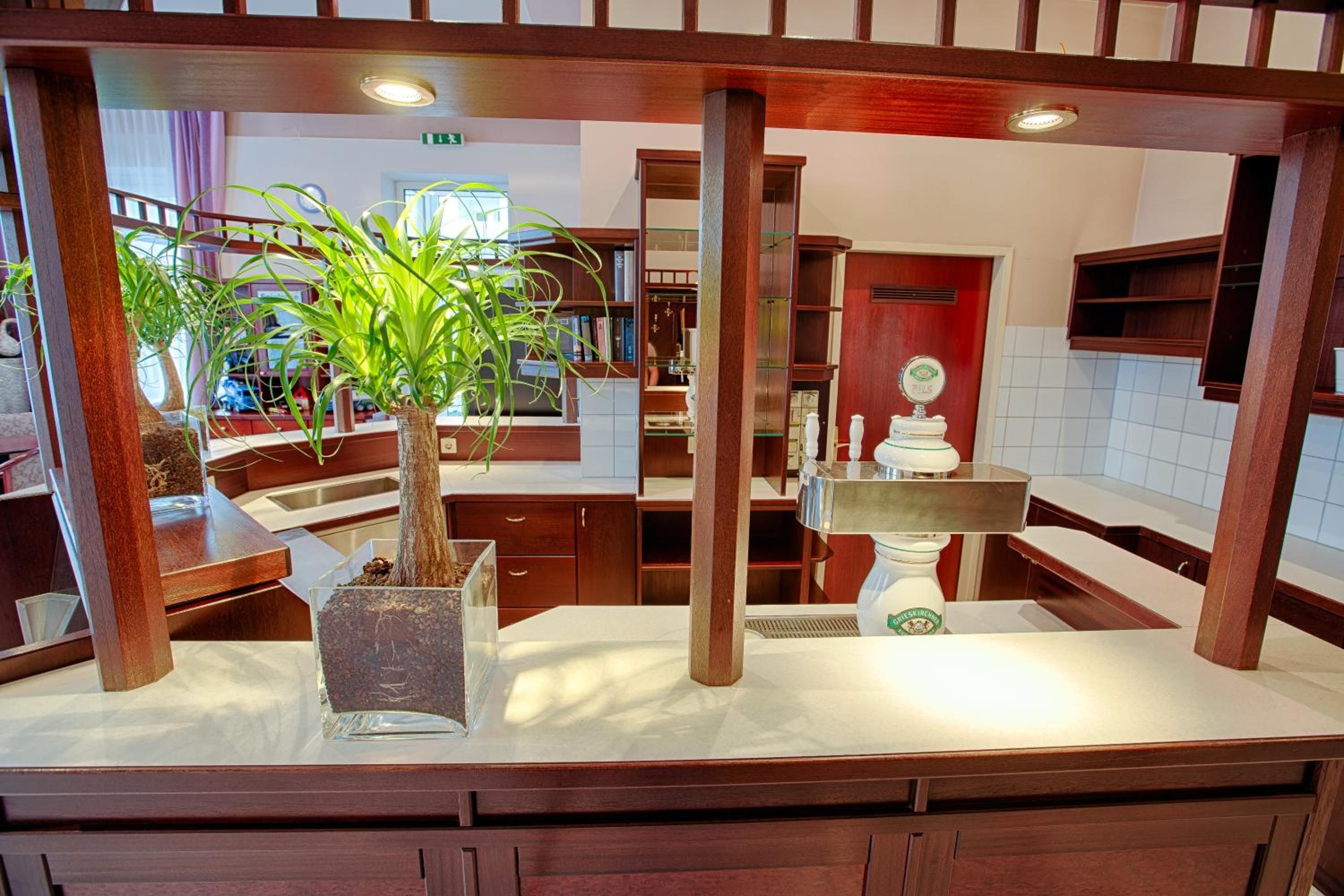 A hotel lobby with a central wooden column, a potted plant, a reception desk, and a decorative fountain.