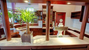 A hotel lobby with a central wooden column, a potted plant, a reception desk, and a decorative fountain.
