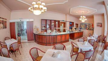 Ein Restaurant mit einer zentralen Bar, mehreren Speisetischen und Stühlen.