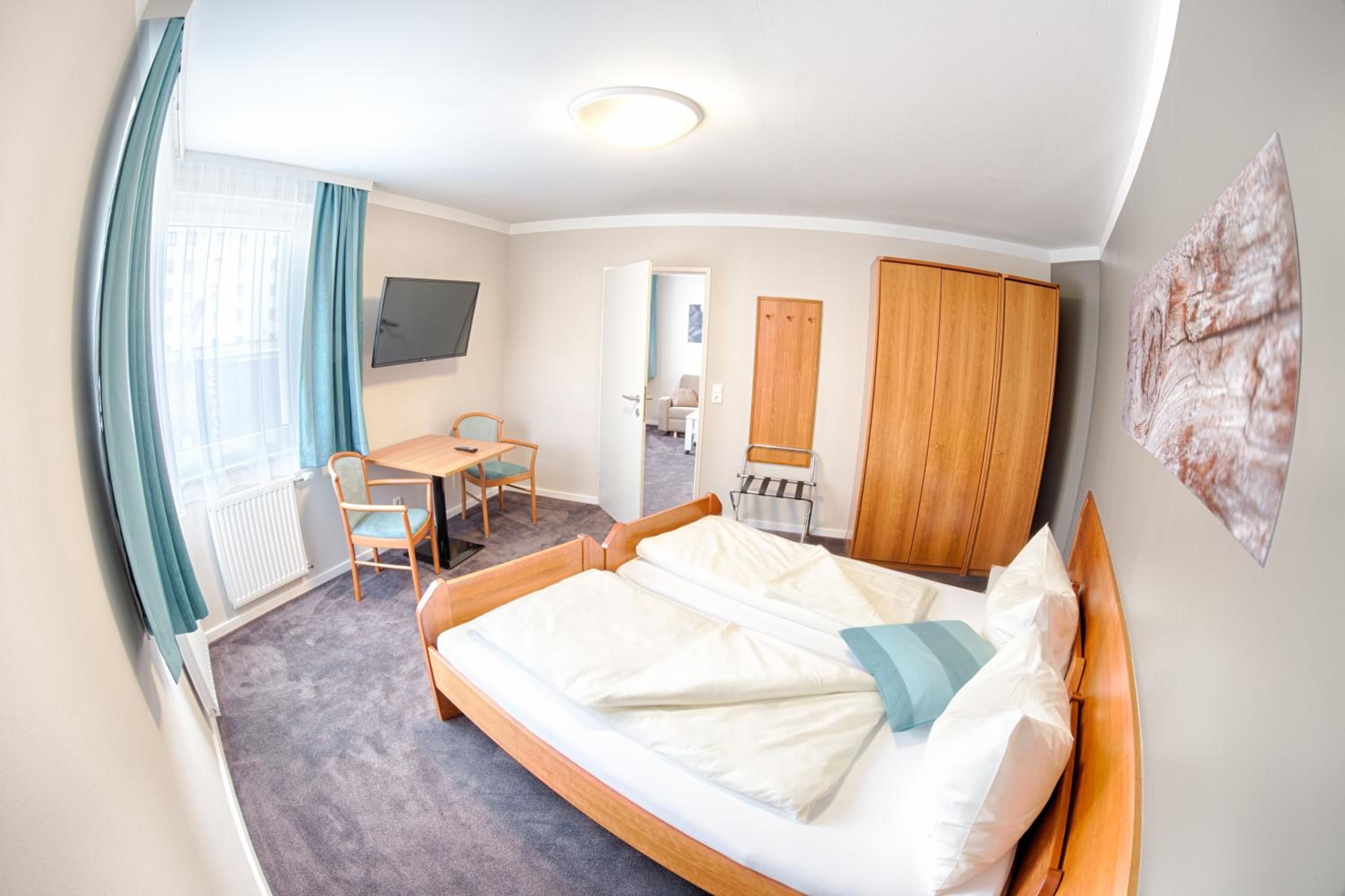 Ein Hotelzimmer mit Bett, Schreibtisch, Stuhl, Kleiderschrank und Fernseher.