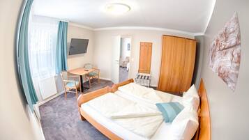Ein Hotelzimmer mit Bett, Schreibtisch, Stuhl, Kleiderschrank und Fernseher.