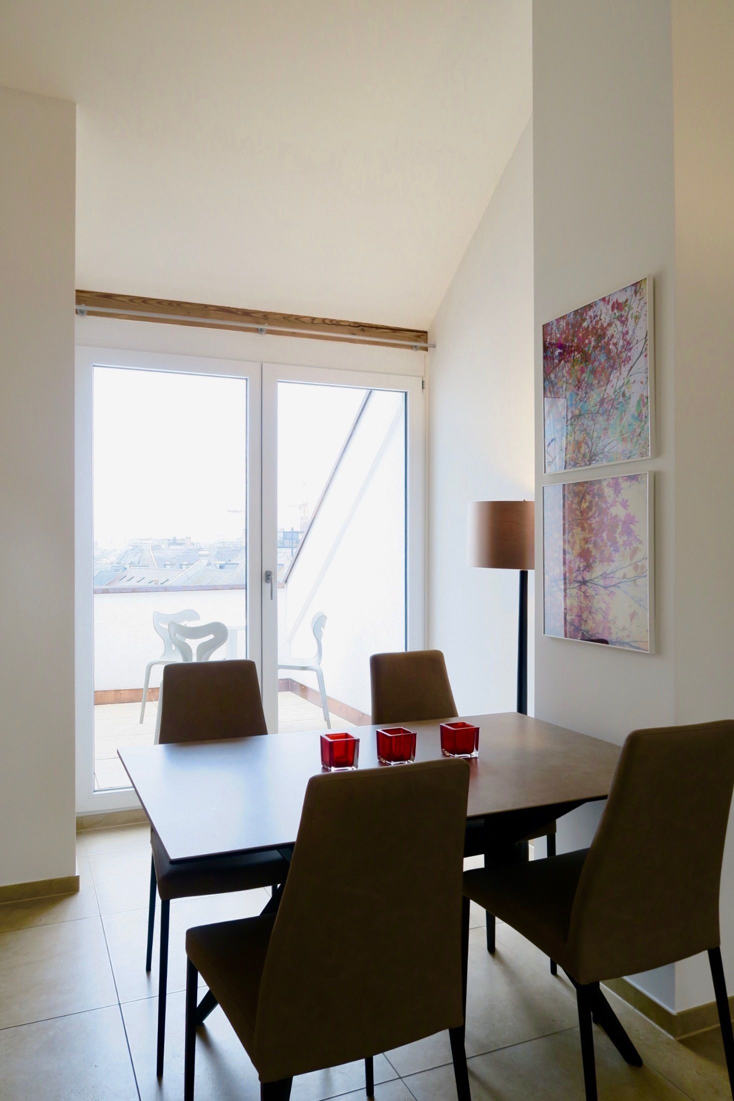 A dining area with a table and chairs, a lamp, and two framed artworks on the wall.