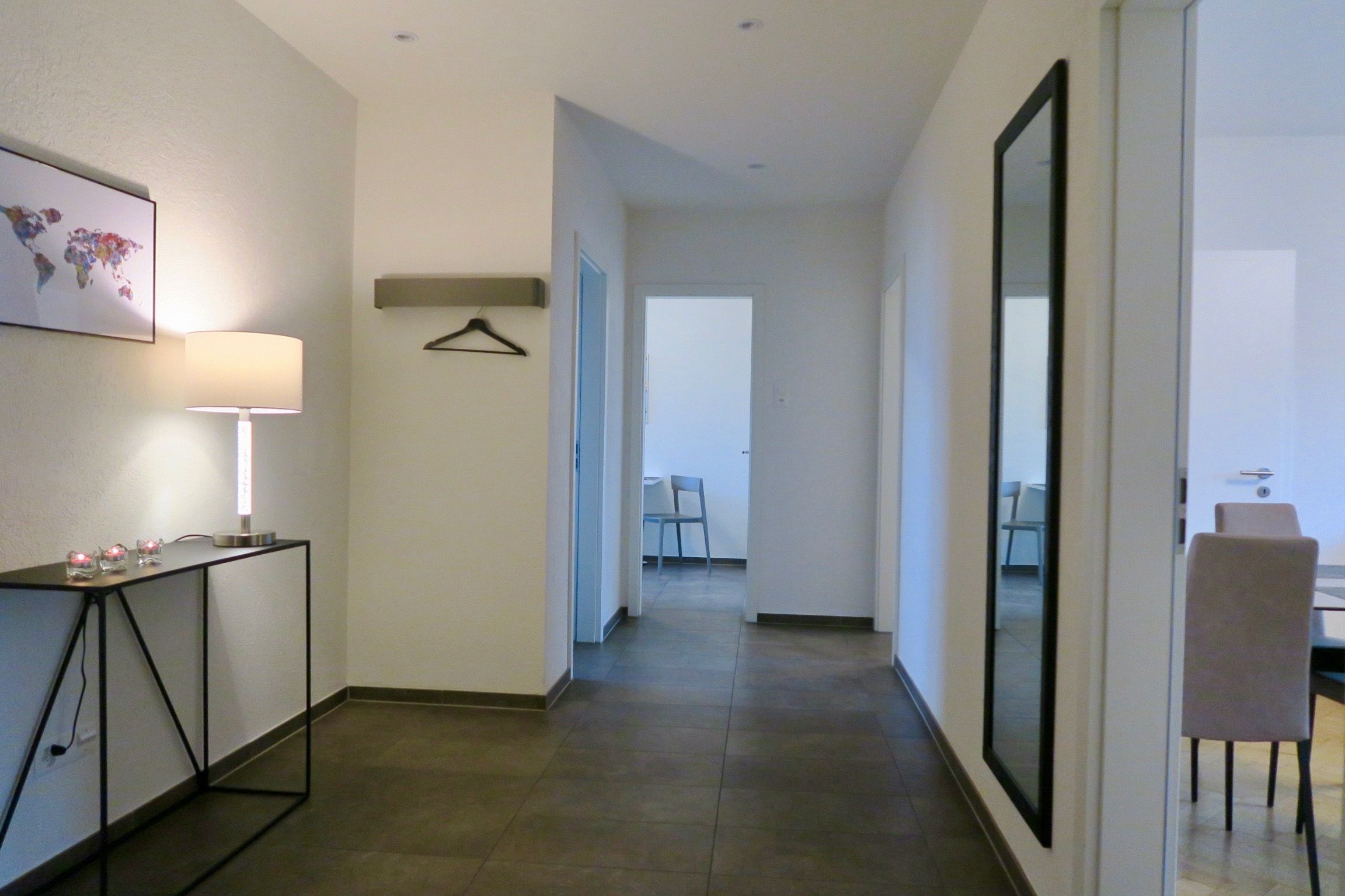 A hallway with a table and chair, a hanging coat rack, and a framed picture on the wall.